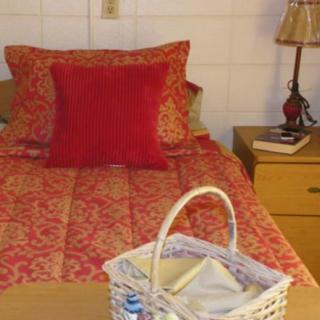 A cozy bedroom setup with a red-themed bedding, a bedside lamp, and a wicker basket on the nightstand.
