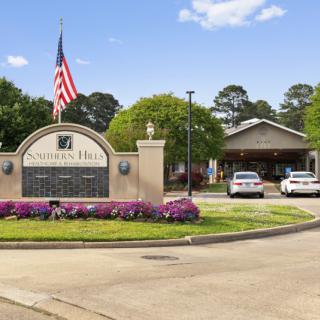 Entrance to a residential building with cars parked in front, featuring an American flag and landscaped surroundings.