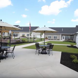 A spacious outdoor patio area with tables and umbrellas set against a backdrop of well-maintained landscaping and buildings.