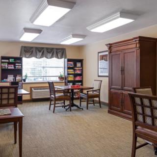 A cozy room with tables and chairs, surrounded by bookshelves and illuminated by overhead lighting.