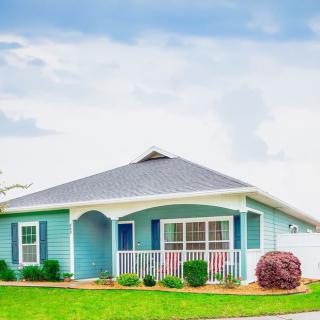 A charming blue bungalow with a well-maintained front yard against a cloudy sky backdrop.