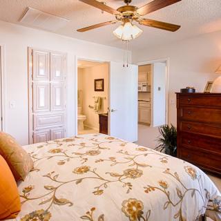 A cozy bedroom with a floral-themed double bed, ceiling fan, and wooden dresser.
