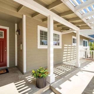 A sunny front porch with a red door, potted plants, and wooden columns casting shadows.