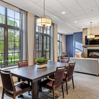 A modern dining and living area with large windows, elegant furniture, and a cozy fireplace.