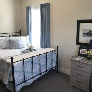 A cozy bedroom with a metal bed frame, adorned with patterned bedding and blue curtains, featuring a nightstand with framed artwork.