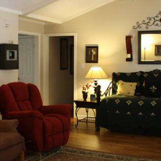 A cozy living room with a red armchair, green sofa, and warm lighting from a table lamp.