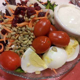 A fresh salad with cherry tomatoes, boiled eggs, seeds, shredded carrots, and a bowl of dressing.