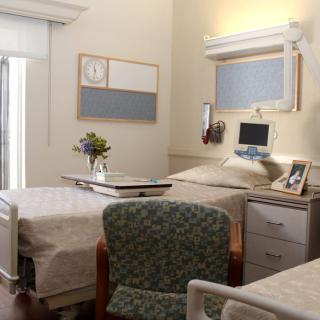 A well-organized hospital room with a bed, chair, and a small table with flowers.