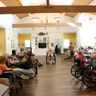 A community room in a nursing home with elderly residents in wheelchairs.