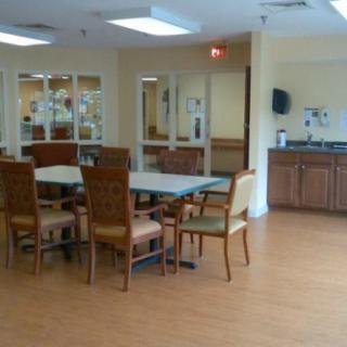 A dining area featuring tables and chairs, with a view of the kitchen in the background.