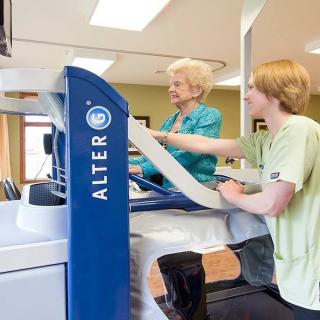 An elderly person undergoing physical therapy using an Alter G treadmill with the assistance of a therapist.