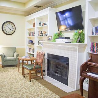 A cozy living room with a fireplace, television, and bookshelf, featuring a comfortable armchair and a piano.