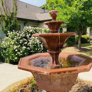 A charming tiered fountain surrounded by vibrant greenery and blooming flowers.