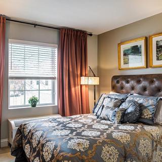 A cozy bedroom with a patterned bedspread, red curtains, and framed artwork.