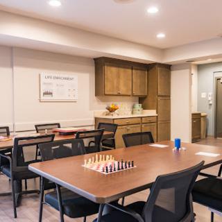 A well-lit meeting room featuring a chess set on the table, surrounded by chairs and wooden cabinetry.