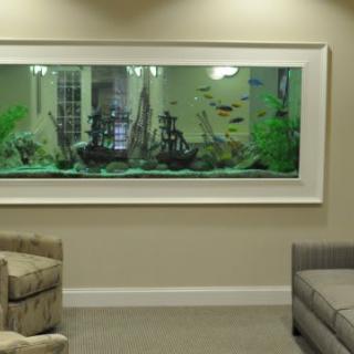 A spacious waiting room featuring a large fish tank set into the wall, accompanied by comfortable seating.