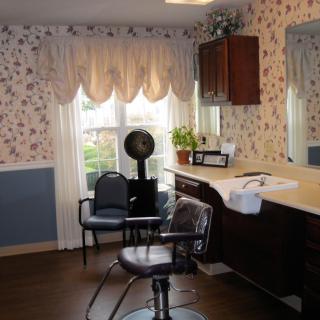 A cozy hair salon with floral wallpaper, a styling chair, and a large window adorned with curtains.