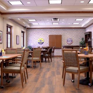 A spacious dining area with neatly arranged tables and chairs, featuring warm lighting and wooden flooring.