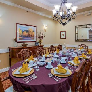 An elegantly set dining room with a chandelier overhead and decorative plates arranged on a table with folded napkins.