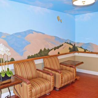 A cozy waiting area with striped armchairs, a mountain mural on the wall, and a wooden floor.