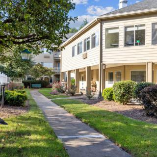 A well-maintained apartment complex with a landscaped yard and a paved pathway under clear skies.