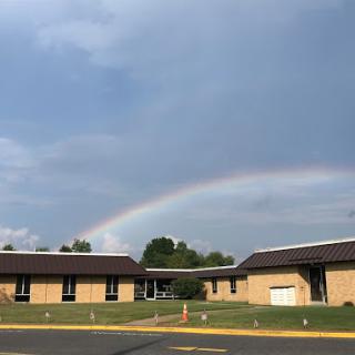 A vibrant rainbow arching over buildings under a cloudy sky.