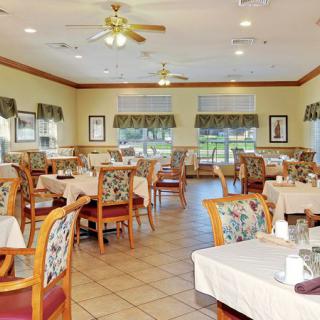 An empty dining area in a restaurant with neatly arranged tables and chairs, featuring large windows and decorative elements.