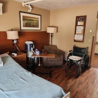 A well-furnished hospital room featuring a bed, an armchair, and a wheelchair.