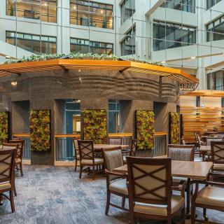 A modern indoor seating area with wooden furniture and greenery accents, located in a well-lit atrium.