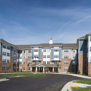 A modern, multi-story apartment building with a circular driveway under a clear blue sky.