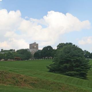 A scenic view of a hill with trees and a distant building under a cloudy sky.