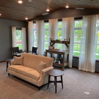 A cozy living room with a sofa, large windows, and elegant curtains.