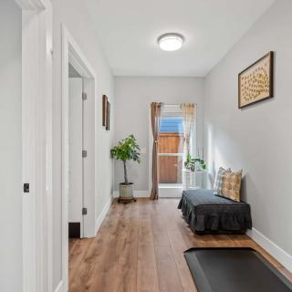 A well-lit hallway with wooden flooring, adorned with a bench, plants, and artwork.
