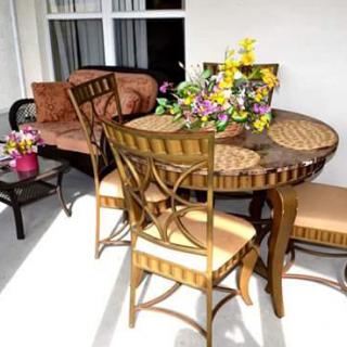 A cozy outdoor patio setup with a wicker table surrounded by chairs, adorned with colorful flowers.