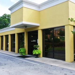 A yellow commercial building with large windows and potted plants at the entrance.