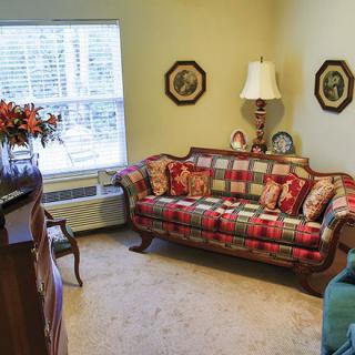 A cozy living room with a patterned sofa, lamp, and floral decor near a large window.