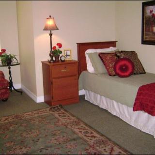 A cozy bedroom with a single bed, nightstand, lamp, and decorative pillows.