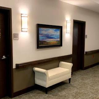 A well-lit hallway featuring a white bench, artwork on the wall, and two doors.
