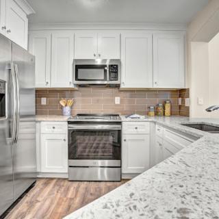 A beautifully designed modern kitchen featuring white cabinetry and sleek stainless steel appliances, complemented by a granite countertop and warm wooden flooring.