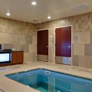 A serene indoor spa area featuring a swimming pool, calming stone walls, and wooden accents.
