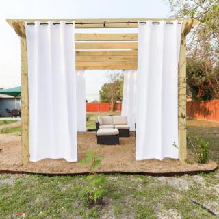 An outdoor pergola with white curtains and patio furniture.