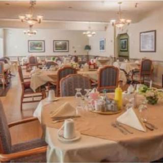 A warmly lit dining room with neatly arranged tables and chairs, featuring elegant chandeliers and a welcoming ambiance.