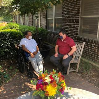 A meaningful conversation takes place in a serene outdoor setting, surrounded by vibrant flowers.