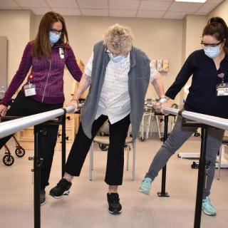 A patient is supported by two therapists while performing rehabilitation exercises in a clinic setting.