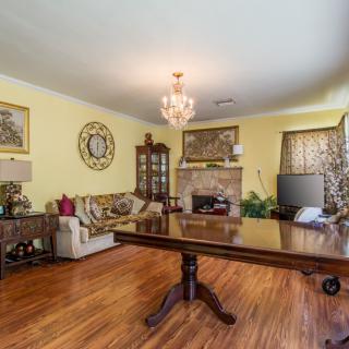 A traditional living room with wooden flooring, featuring a chandelier, sofa, table, fireplace, and cabinet.