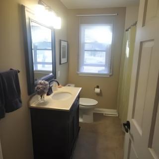 A narrow bathroom with a sink, mirror, toilet, and window.