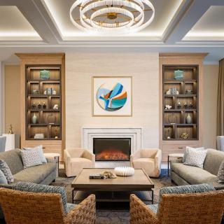 A modern living room featuring a central fireplace, surrounded by plush seating and elegant shelving, adorned with contemporary artwork and lighting.