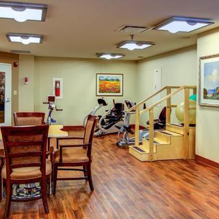 A cozy exercise room with gym equipment, wooden flooring, and seating area.