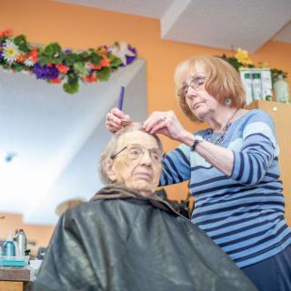 A hairdresser styling an elderly woman's hair in a salon.