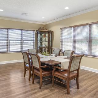 A well-lit dining room with a wooden table and six chairs, surrounded by large windows and featuring a hardwood floor.